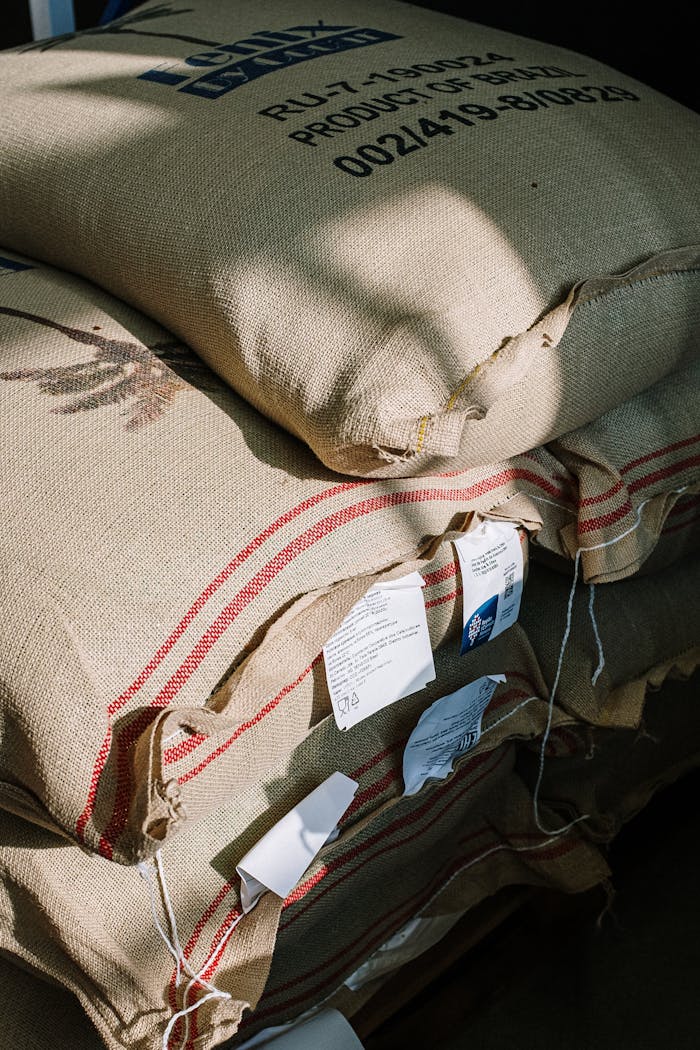 Stack of burlap sacks filled with organic coffee beans in a roastery, captured with natural light.