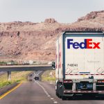 A FedEx truck travels on a scenic highway through Arizona's desert landscape under a clear sky.