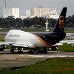 UPS cargo aircraft taxiing on runway at an airport with cityscape background.